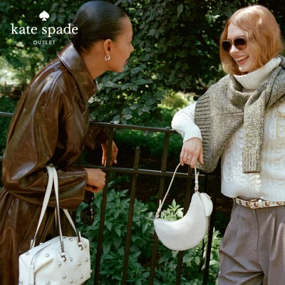 Two women with Kate Spade handbags chatting by an iron fence